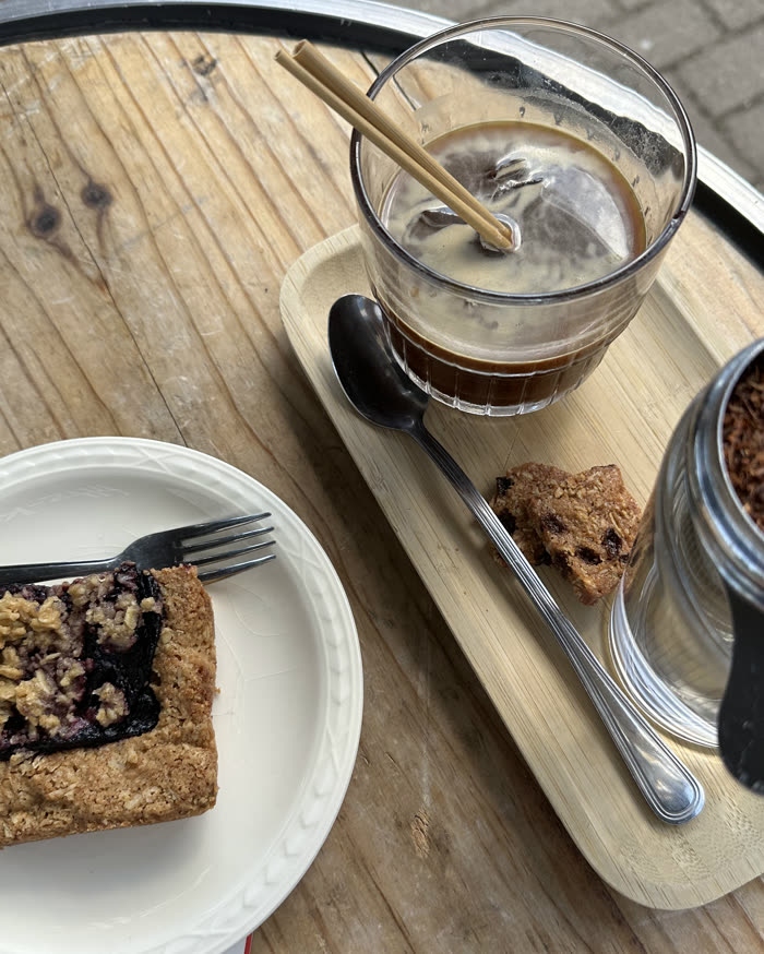 Iced coffee and a slice of crumble cake on a wooden tray