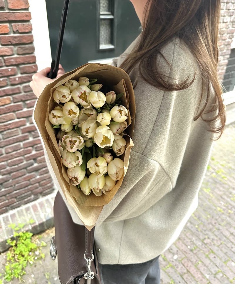 A bunch of cream tulips in kraft paper, carried against a wool coat